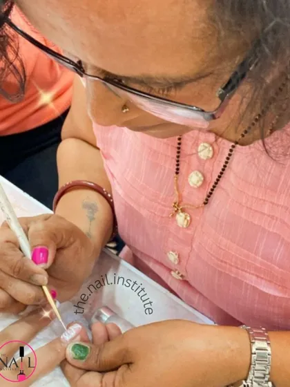 A student practices her brush strokes, creating a glittery design on a practice nail.