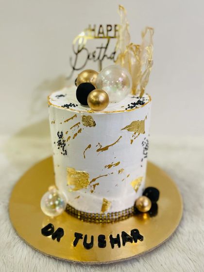 A tall, modern cake with a white and gold leaf design. The black and gold spheres and abstract sails on top give it a sophisticated, artistic feel.