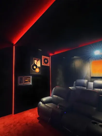 Welcome to a private home theater designed for an immersive cinematic experience. The room features plush leather recliners, professional acoustic treatment, and dramatic red and black decor with adjustable mood lighting to create the ultimate entertainment escape.