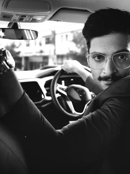 A candid, in-car portrait of actor Ali Fazal. This black and white shot creates a timeless, cinematic feel, capturing a moment of connection between the subject and the camera.
