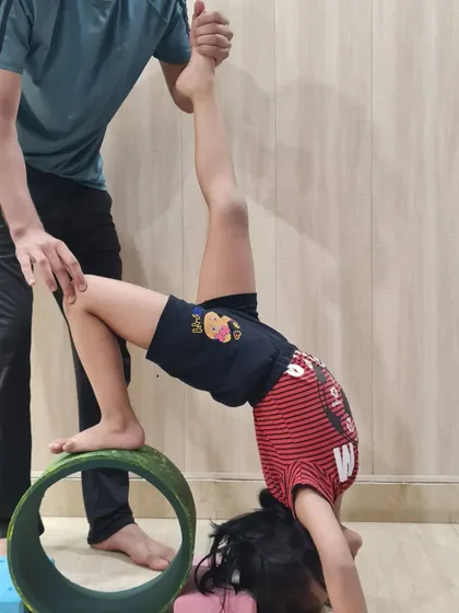 Using props like the yoga wheel, we can safely guide children into deeper stretches. This student is practicing an assisted one-legged wheel pose, which builds core strength and improves balance.