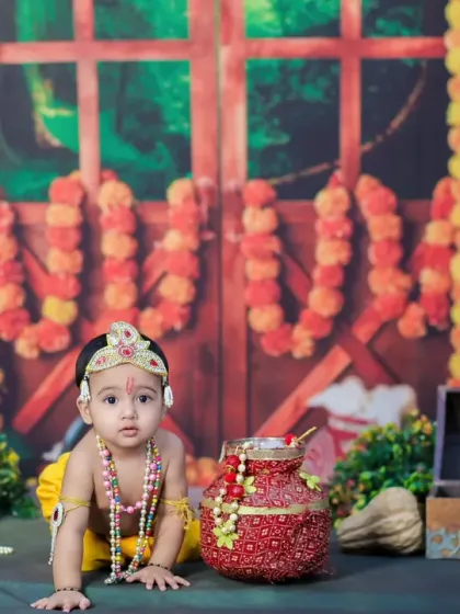 This Little Krishna looks directly at the camera with an innocent gaze. The setup includes a backdrop of a temple door adorned with marigold garlands.