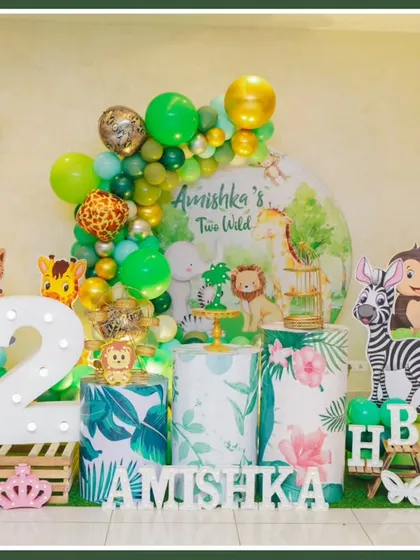 A "Two Wild" jungle theme for a second birthday. This setup features a clean white backdrop, cute animal cutouts, and a green and gold balloon arch.