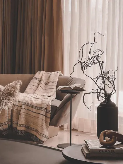 This cozy corner showcases the beauty of texture, with a soft throw blanket, pampas grass, and a sculptural vase creating a warm and inviting vignette.