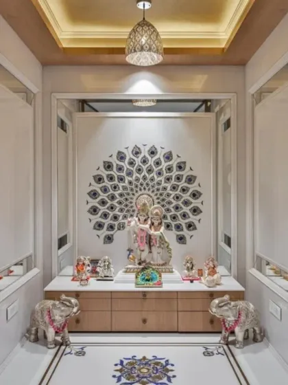 This elegant pooja room combines classic and contemporary elements, featuring a detailed peacock feather inlay on a marble wall. The space is symmetrically designed with silver elephant statues, a modern pendant light, and ample storage in the base cabinet.