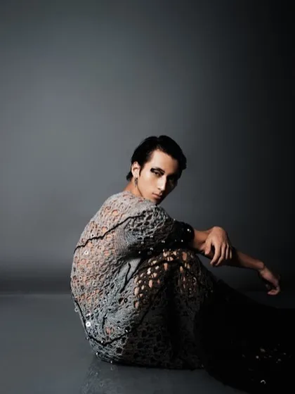 This shot captures the full effect of the avant-garde grooming, with the model's pose highlighting the dramatic eye makeup and the texture of the unique, deconstructed garment.