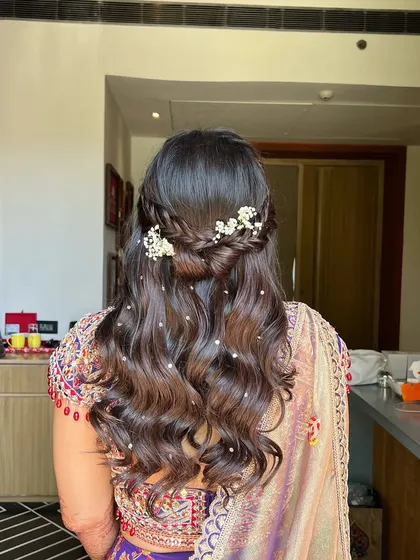 A delicate half-updo for a Haldi function, featuring a fishtail braid and small pearls scattered through the soft waves.