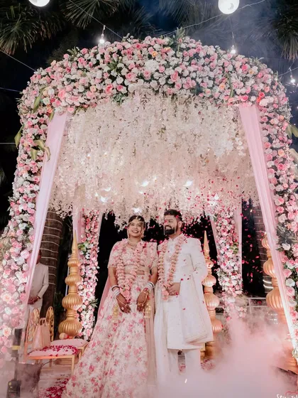 A dreamy pastel mandap enveloped in smoke effects for a magical varmala. The combination of soft pink florals, cascading white wisterias, and ethereal fog creates a truly romantic and unforgettable atmosphere.