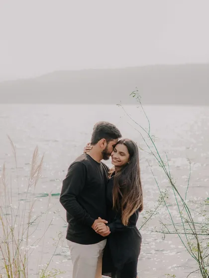 An intimate embrace by the water's edge. The sparkling water and hazy mountains in the background create a dreamy, romantic backdrop for this couple's portrait.
