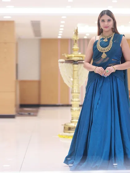 A full-length shot of a model in a blue half-saree, taken during a collaboration with a jewellery brand. The clean, well-lit environment of the showroom allows the gold jewellery to shine.