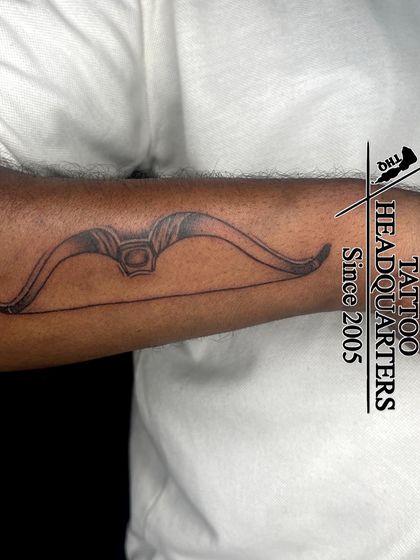 A bow and arrow tattoo, often symbolizing focus, direction, and strength, inked on the forearm.