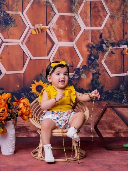 This little one is celebrating her first birthday with a fun bee-themed photoshoot. The "ONE" blocks and cheerful yellow props make for a bright and happy setting.