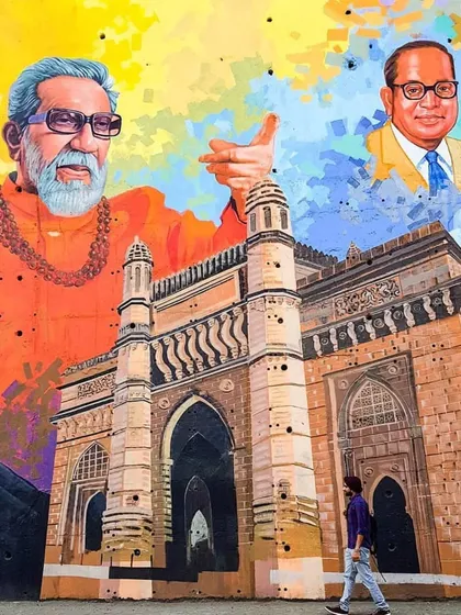 A person walks past the vibrant mural depicting Mumbai's cultural and political figures. This shot gives a sense of the scale of the artwork and how it integrates into the daily life of the street.