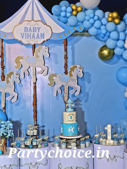 A full view of a carousel-themed party at night by the pool. The setup is beautifully lit, with the cake and desserts displayed on themed pedestals in front of the main backdrop.