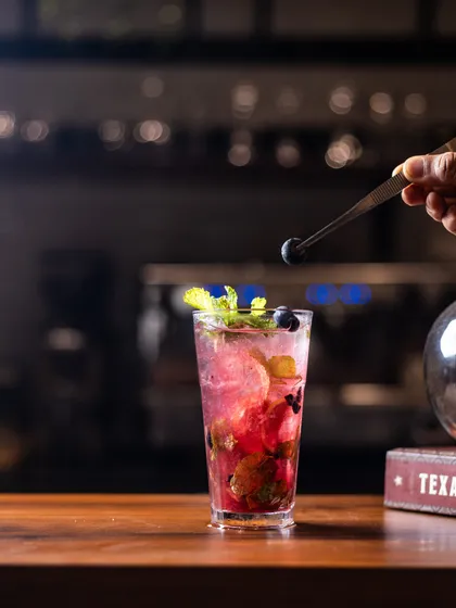 A bartender carefully adds a fresh blueberry as the final touch to this bubbly, berry-filled mocktail. It’s the small details that make a drink special.