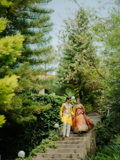 The couple descending a staircase hand-in-hand, surrounded by lush greenery. A beautiful, candid moment from their Haldi day.