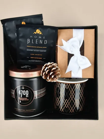 A simple yet elegant 'Cozy at Home' hamper. This version includes premium coffee blend packets, gourmet popcorn, and a patterned mug, all neatly arranged in a black gift box.