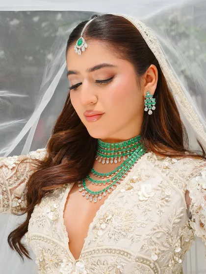 An ethereal bridal look in ivory, accented with emeralds. The makeup is fresh and radiant, with a focus on a dewy complexion and soft pink tones to complement the modern bride's aesthetic.