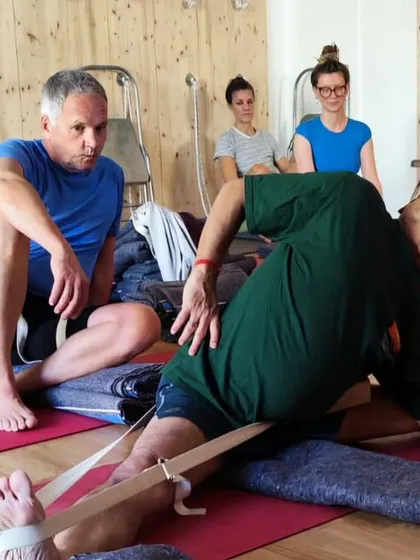 A moment of teaching and adjustment during a workshop, focusing on a deep seated forward bend.