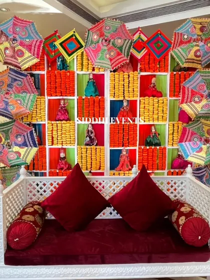 This seating area combines comfort with vibrant tradition. A classic white wooden swing is set against a colorful backdrop of marigold garlands, Rajasthani kathputli puppets, and decorative umbrellas, creating a perfect, culturally rich photo opportunity for guests.