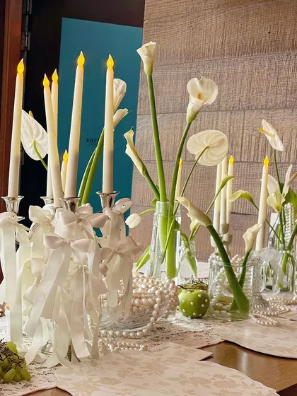 A beautiful tablescape with white calla lilies, taper candles adorned with ribbons, and scattered pearls.