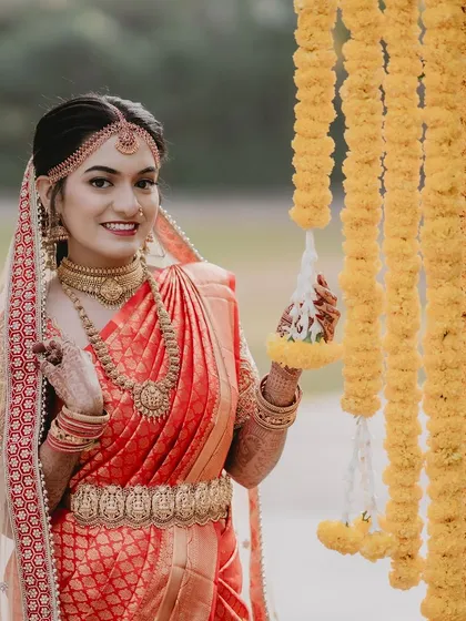 The lovely Tanu posing with traditional marigold decorations, her red bridal saree and gold jewellery shining.