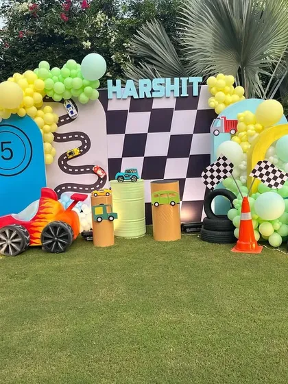 I created this action-packed car race theme for a 5th birthday party in a garden setting. The setup includes a checkered flag backdrop, custom racetrack cutouts, tire props, and a vibrant balloon arch in green, yellow, and blue.