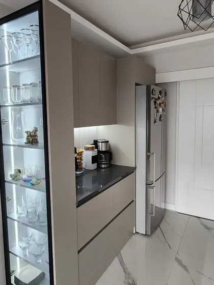 This view shows the crockery unit next to a tall, glass-fronted display cabinet. The cabinet has internal LED strips on each shelf, beautifully illuminating the glassware inside.