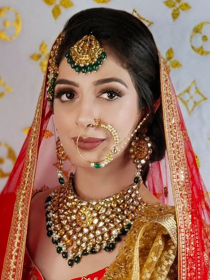 A bride wearing a heavy Polki choker with green beads. The set is paired with a red and gold lehenga, a classic and unbeatable combination.