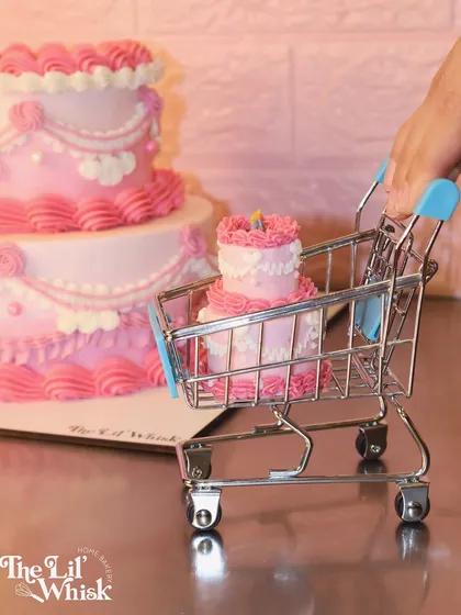 Your dream birthday cake is ready to be added to your cart. This shot playfully features a miniature version of our tiered pink vintage cake in a tiny shopping cart.