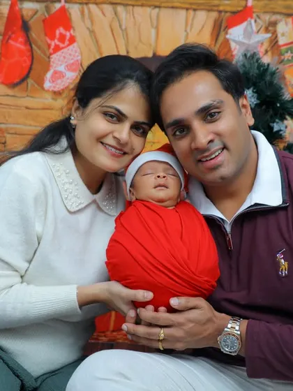 A precious moment with a newborn wrapped in red, held by both parents against a festive Christmas backdrop. This photo captures the warmth and joy of a family's first holiday season together.