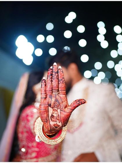 A creative shot where the bride's portrait mehendi on her hand aligns with her and her groom in the background. A beautiful memory captured.
