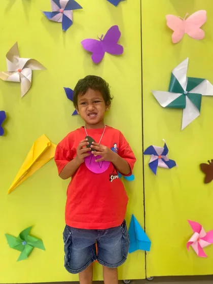 A student shows off his craft medal in front of a wall decorated with pinwheels and butterflies. Our sessions always include a creative outlet for the children.