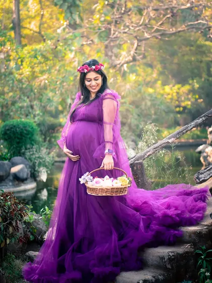 A fairytale-like portrait of the mom-to-be in a stunning purple gown, walking down a stone path with a basket of flowers.
