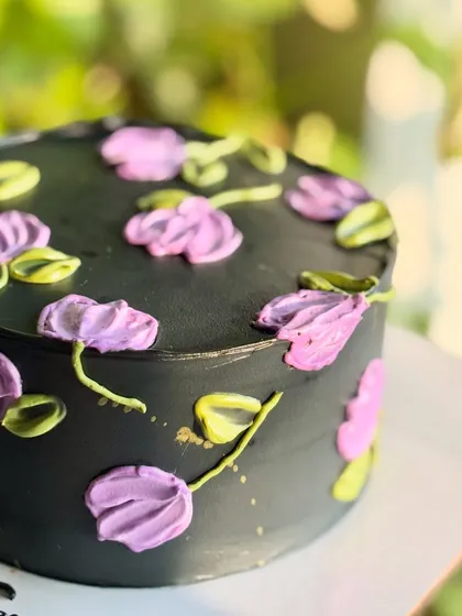 A detailed shot of the black floral cake, focusing on the texture and color variation in the palette knife flowers and the subtle gold splatter.