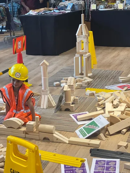 I believe in the power of play, and our dedicated kids' zones are designed for exactly that. Here, a young engineer is completely absorbed in building with giant wooden blocks, an example of the open-ended, creative fun I arrange to keep your children happily engaged.