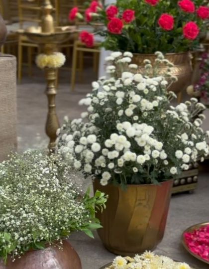 An assortment of fresh flowers, including baby's breath and white chrysanthemums, arranged in traditional brass and copper pots.