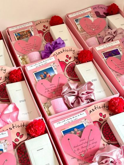A token of love for your bridesmaids. This hamper includes a personalized heart-shaped neckpiece, a satin scrunchie, a Zara pocket perfume, a scented candle, and a face sheet mask, all beautifully arranged in a pink box.