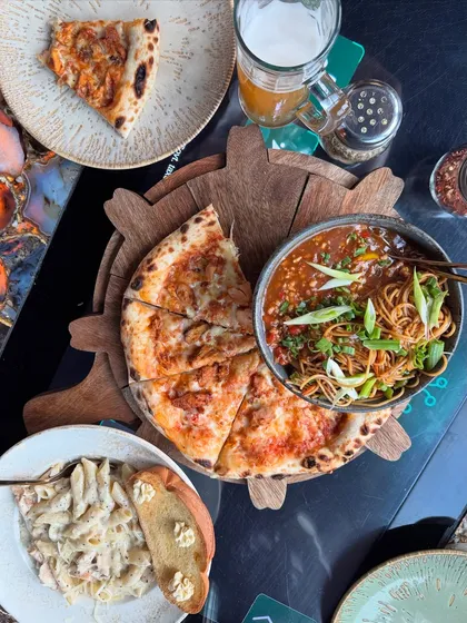 A perfect flat lay showcasing a delicious spread at a trendy Noida cafe. I focus on making the food look as good as it tastes, capturing everything from wood-fired pizza and savory noodles to creamy pasta, encouraging my audience to save the spot for their next meal.