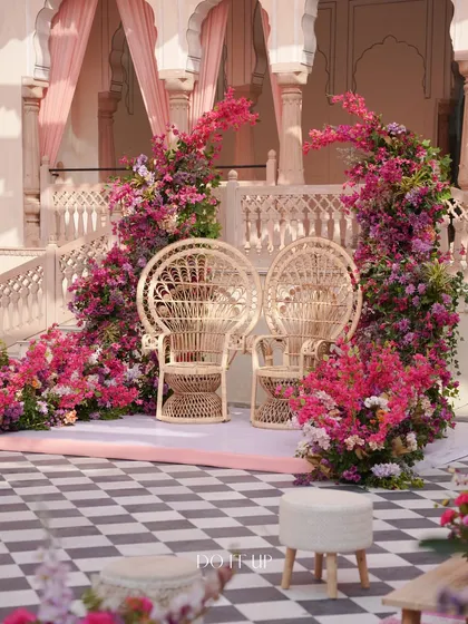 The main seating for the couple at the Jaipur Haldi. Two peacock chairs are framed by dramatic, cascading arrangements of pink bougainvillea, creating a stunning floral throne.
