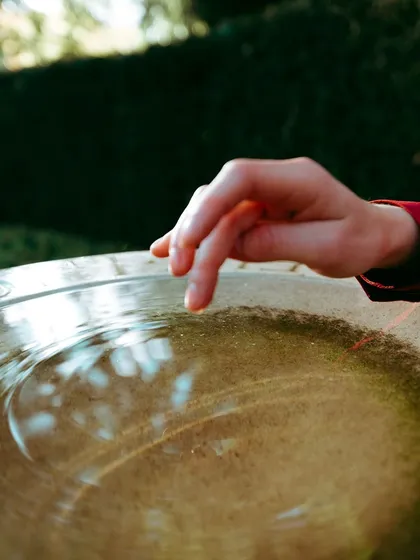 A detailed shot focusing on a hand touching the surface of water, capturing the delicate ripples and reflections in an outdoor setting.