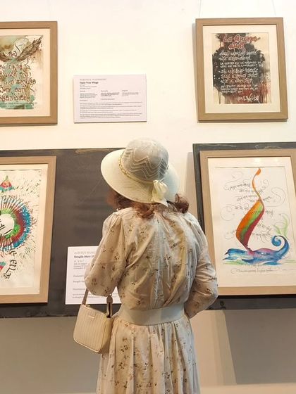 A visitor dressed in vintage attire admires the calligraphic art, her outfit complementing the elegance of the exhibition. Our gallery attracts a diverse and culturally engaged audience.