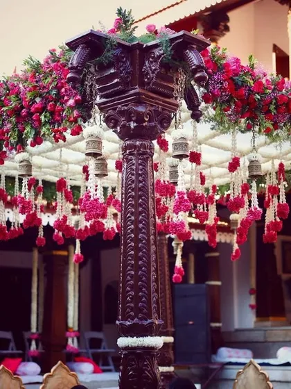 A close-up of the intricately decorated mandap at the Thottimane venue, showing the rich red flowers and hanging white floral strings with brass bells.
