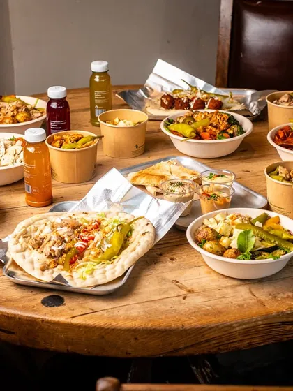 A huge spread of Middle Eastern takeaway food on a rustic wooden table. This shot conveys a sense of feasting and abundance.
