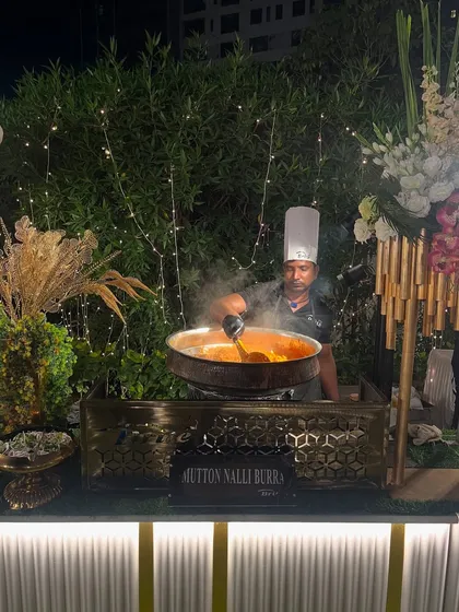 A chef prepares a large batch of Mutton Nalli Burra at a live cooking station. The rising steam and rich aroma of this traditional Mughlai dish create an immersive and memorable experience for guests.