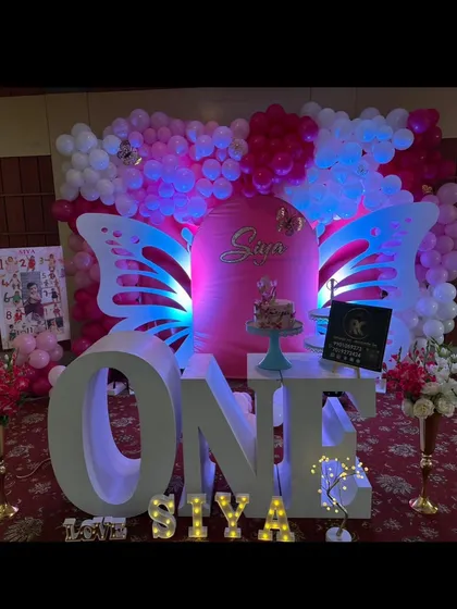 A wide shot of a butterfly-themed first birthday, featuring large illuminated wings and 'ONE' letters. The pink and white color scheme creates a soft and beautiful ambiance.