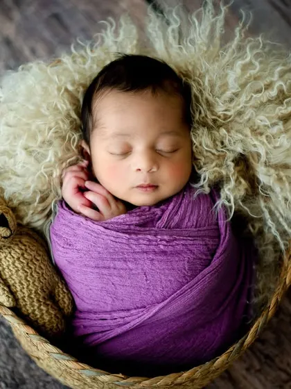 Showcasing a pop of color with this rich purple wrap. The baby is nestled on a soft fur rug in a woven basket, accompanied by a little teddy bear friend for a classic newborn photo.