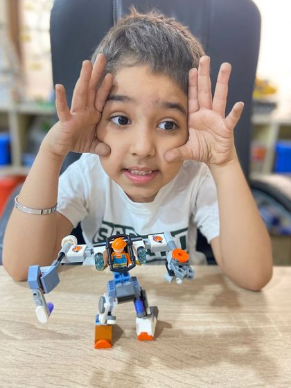 A student poses playfully with his custom-built LEGO robot, a product of his own imagination and our free-building sessions.