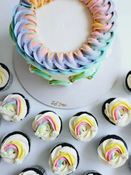 A different take on the rainbow theme. This unique letter "O" cake is decorated with beautiful pastel rainbow piping and surrounded by matching rainbow cupcakes, offering a creative twist for a birthday celebration.
