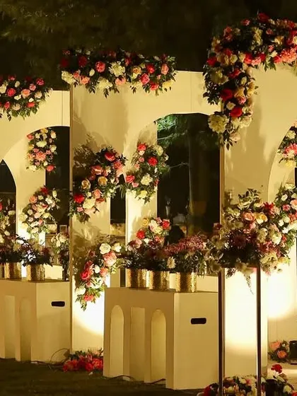 A wide shot of the romantic reception entrance, with a long wall of white arches adorned with beautiful pink and red flowers.